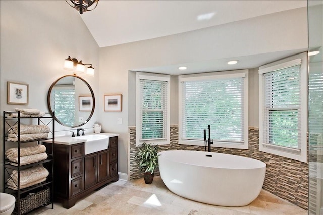 bathroom featuring vanity, a soaking tub, tile walls, and vaulted ceiling