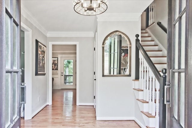 foyer with ornamental molding, stairway, light wood finished floors, baseboards, and a chandelier