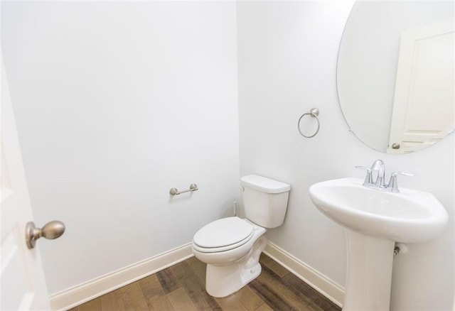 half bathroom with baseboards, wood finished floors, toilet, and a sink