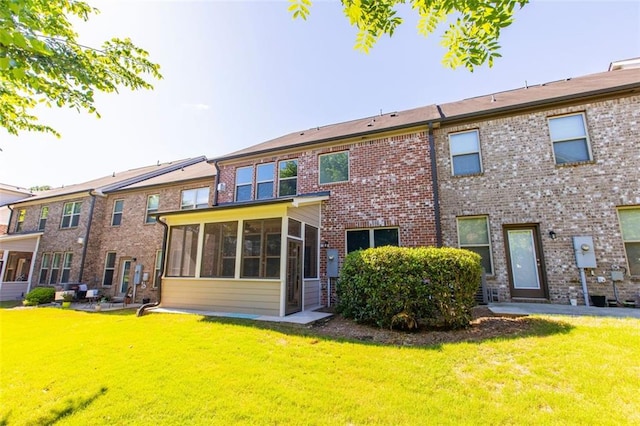 back of house featuring a sunroom, a lawn, and brick siding