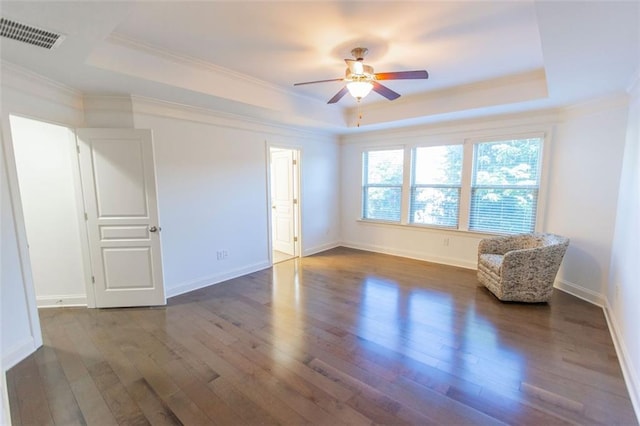 empty room with a tray ceiling, crown molding, dark wood finished floors, a ceiling fan, and baseboards