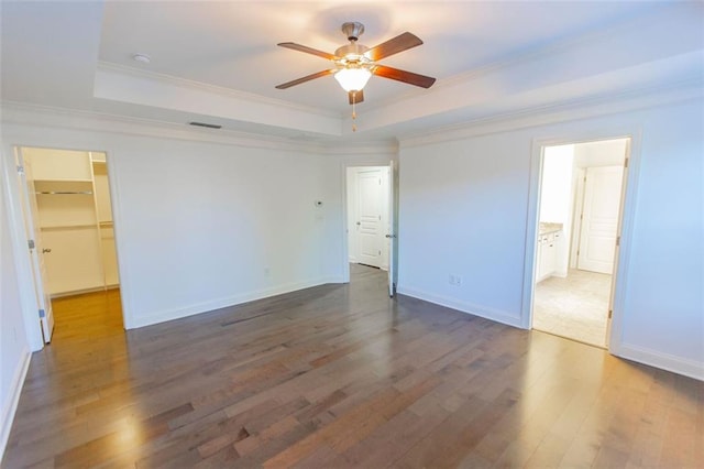 unfurnished bedroom featuring a raised ceiling, wood finished floors, ornamental molding, a walk in closet, and baseboards