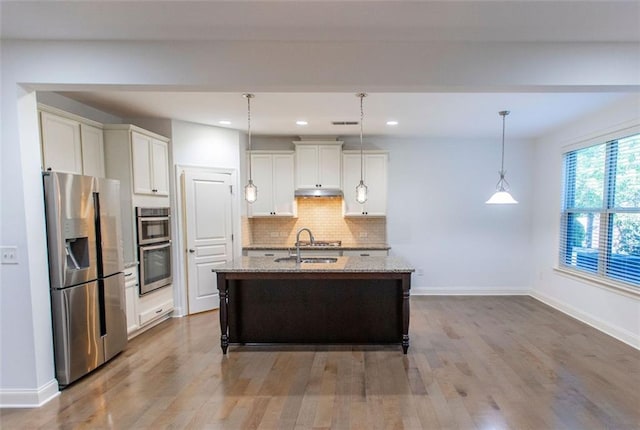 kitchen featuring stainless steel appliances, light stone counters, tasteful backsplash, wood finished floors, and baseboards