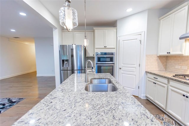 kitchen featuring appliances with stainless steel finishes, a sink, white cabinets, decorative light fixtures, and tasteful backsplash