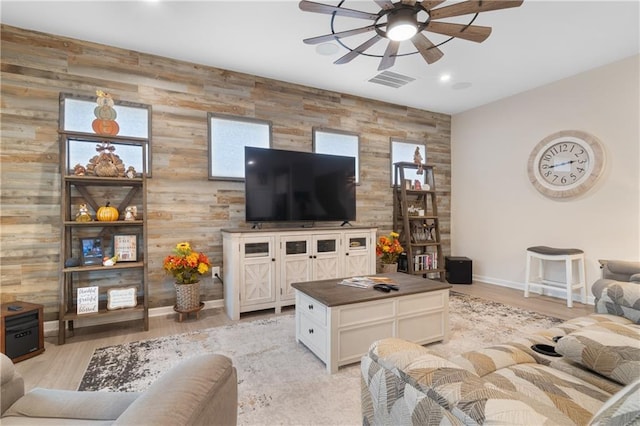 living room featuring light wood-type flooring, wood walls, and ceiling fan