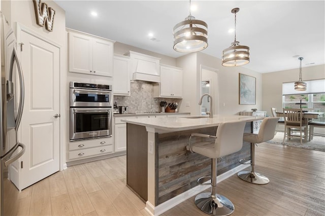 kitchen with white cabinets, hanging light fixtures, sink, light hardwood / wood-style flooring, and stainless steel appliances