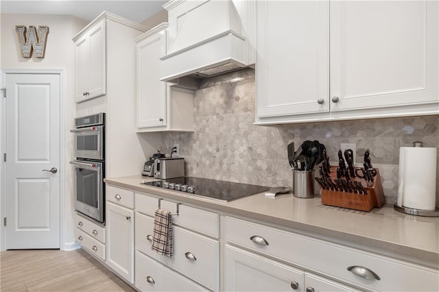 kitchen featuring black electric stovetop, white cabinetry, double oven, and premium range hood