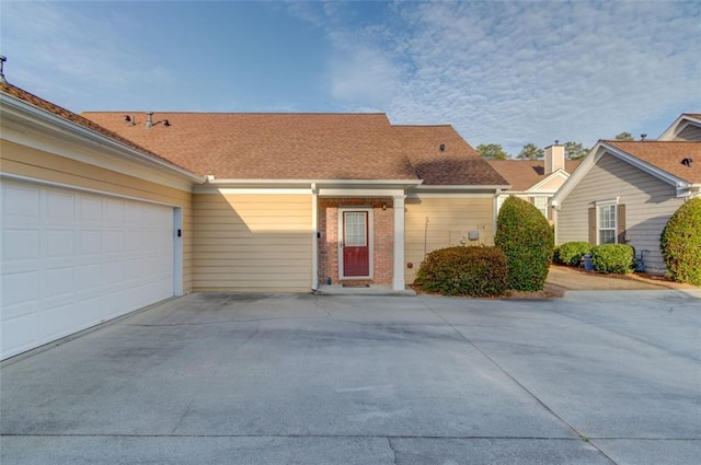 ranch-style house with a garage, driveway, roof with shingles, and brick siding