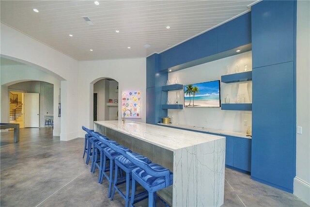 kitchen featuring blue cabinetry, a center island with sink, a kitchen bar, and light stone counters