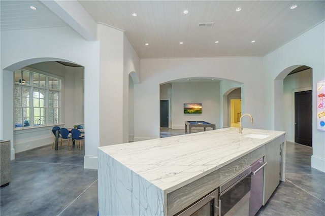 kitchen with an island with sink, light stone counters, and sink