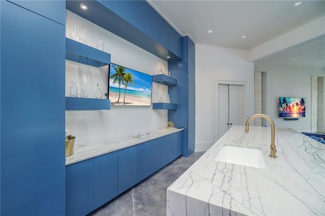 interior space with concrete floors, sink, blue cabinets, and light stone counters