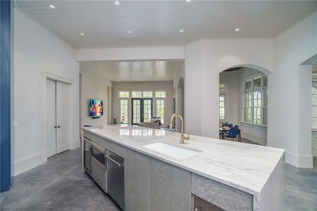 kitchen with sink, light stone counters, a center island with sink, and dishwasher