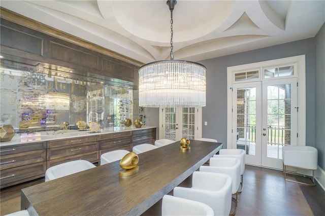 dining room featuring a raised ceiling, dark wood-type flooring, a chandelier, and french doors