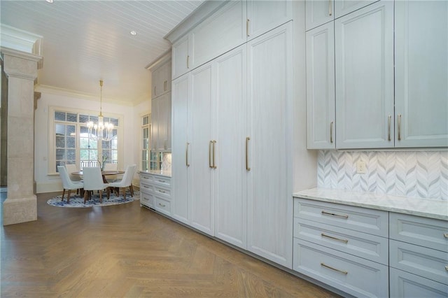 kitchen with hanging light fixtures, light stone counters, a notable chandelier, parquet floors, and crown molding