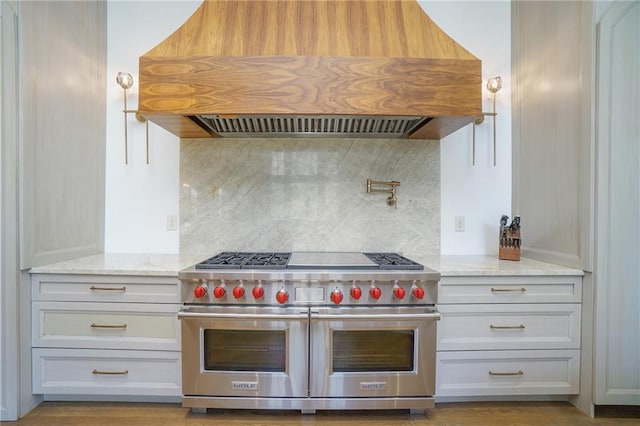 kitchen with custom range hood, tasteful backsplash, light stone counters, double oven range, and white cabinets