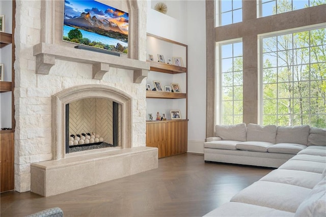 living room featuring built in shelves, a stone fireplace, dark parquet flooring, and a wealth of natural light