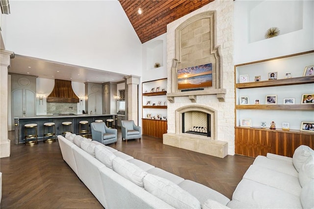 living room with a high ceiling, dark parquet floors, decorative columns, and a fireplace