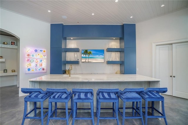 kitchen featuring light stone countertops, a kitchen island with sink, a kitchen bar, and blue cabinetry