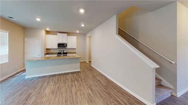 kitchen featuring stainless steel appliances, white cabinets, light stone counters, light hardwood / wood-style flooring, and a kitchen island with sink