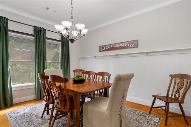 dining space with light wood-type flooring, an inviting chandelier, and ornamental molding