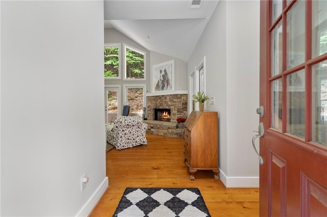 foyer entrance with lofted ceiling, a stone fireplace, and light wood-type flooring