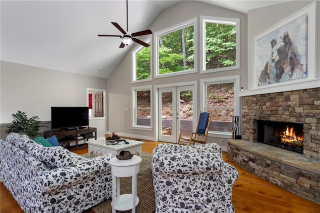 living room featuring hardwood / wood-style floors, french doors, a stone fireplace, high vaulted ceiling, and ceiling fan