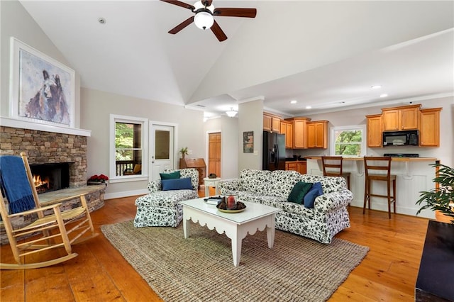 living room with vaulted ceiling, ceiling fan, light hardwood / wood-style flooring, and a stone fireplace