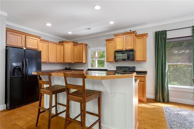 kitchen with black appliances, a kitchen island, a kitchen bar, light hardwood / wood-style floors, and ornamental molding