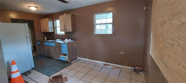 kitchen with light brown cabinetry, sink, white fridge, and light tile patterned floors