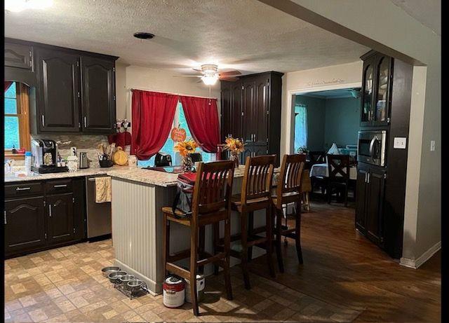 kitchen featuring ceiling fan, a textured ceiling, stainless steel appliances, a kitchen bar, and decorative backsplash