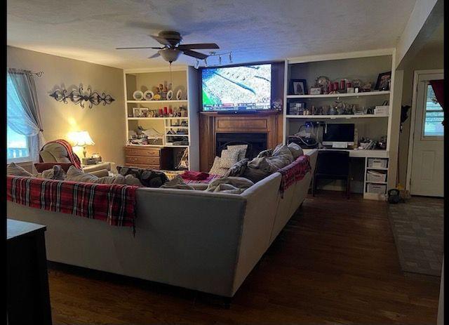 living room with ceiling fan, a textured ceiling, dark wood-type flooring, and a healthy amount of sunlight