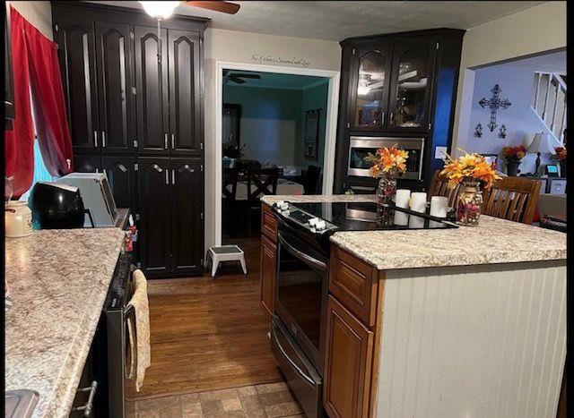 kitchen featuring dark brown cabinetry, ceiling fan, dark hardwood / wood-style floors, a center island, and electric stove