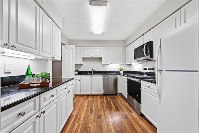 717 Beaufort Cir, Duluth, GA 30096 - kitchen with stainless steel appliances, a sink, white cabinetry, dark countertops, and wood finished floors