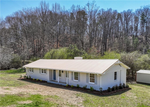 ranch-style house with a front lawn, a porch, metal roof, brick siding, and a chimney