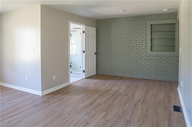 unfurnished room with built in shelves, wood finished floors, baseboards, and brick wall