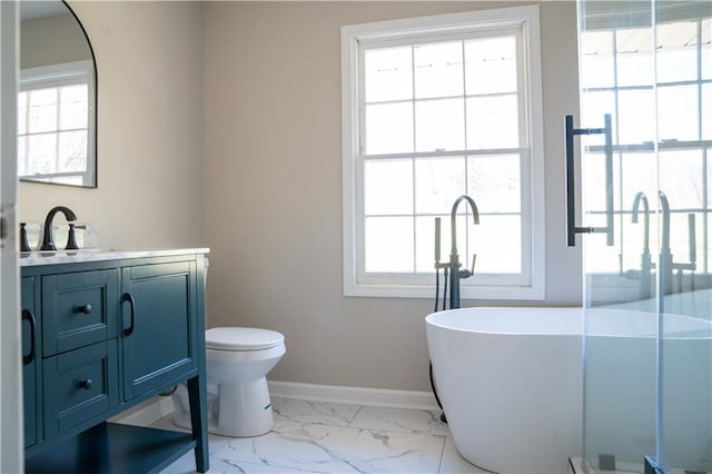 full bath with a freestanding tub, toilet, marble finish floor, baseboards, and vanity