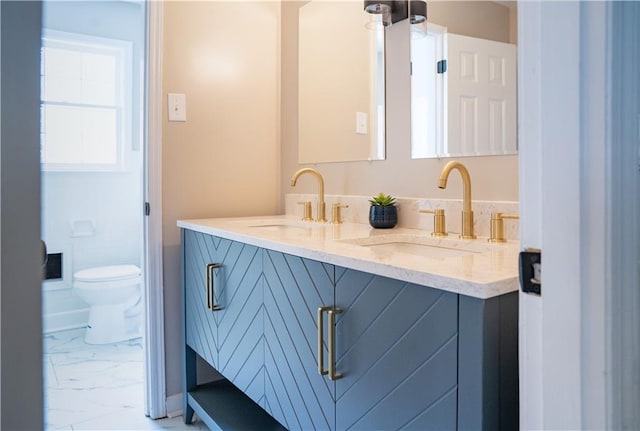 full bathroom featuring a sink, toilet, marble finish floor, and double vanity