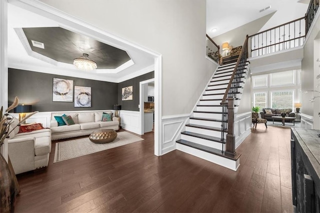 living room featuring dark wood-style floors, a tray ceiling, wainscoting, and stairway