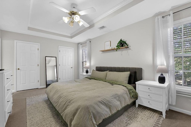 carpeted bedroom with a raised ceiling, multiple windows, ceiling fan, and crown molding