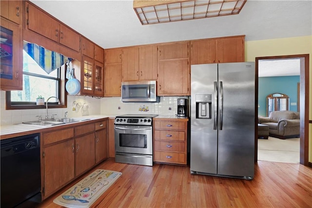 kitchen with brown cabinetry, light wood finished floors, a sink, appliances with stainless steel finishes, and tasteful backsplash