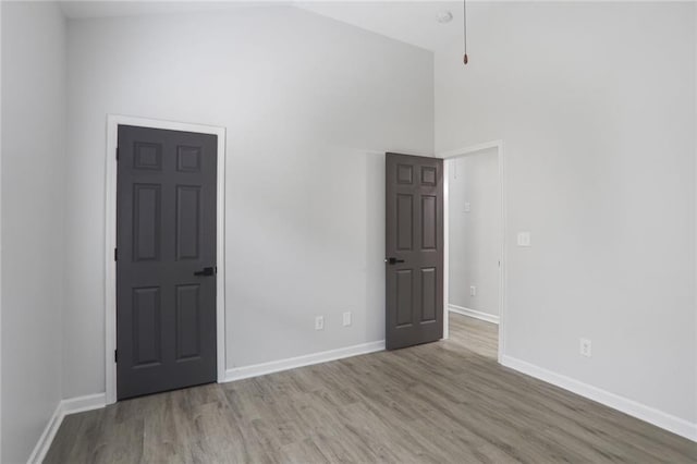 unfurnished room featuring high vaulted ceiling, baseboards, and wood finished floors