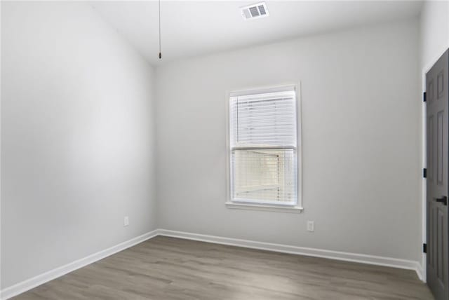 empty room featuring wood finished floors, baseboards, and visible vents