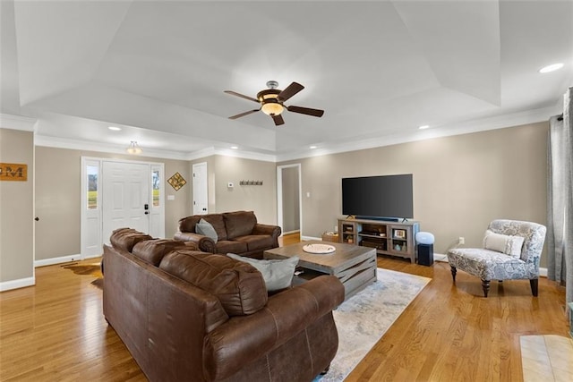 living room with light wood-style floors, a tray ceiling, and baseboards