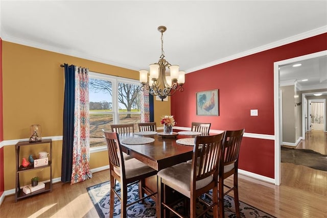 dining space with ornamental molding, a notable chandelier, baseboards, and wood finished floors