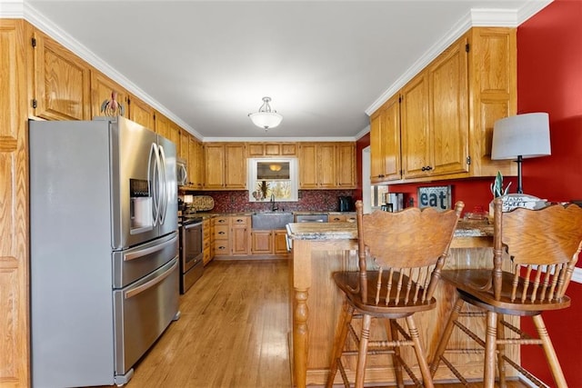 kitchen with light wood-style flooring, a sink, appliances with stainless steel finishes, brown cabinetry, and a kitchen bar