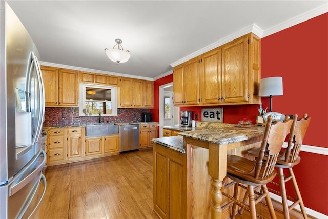 kitchen featuring light wood finished floors, appliances with stainless steel finishes, a peninsula, crown molding, and a sink