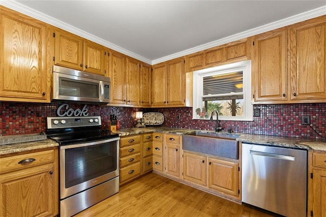 kitchen with stainless steel appliances, a sink, light wood finished floors, dark stone countertops, and tasteful backsplash