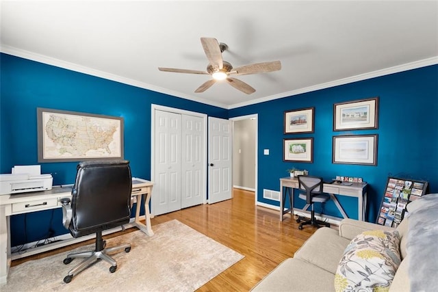 office space with a ceiling fan, baseboards, visible vents, light wood-style floors, and ornamental molding