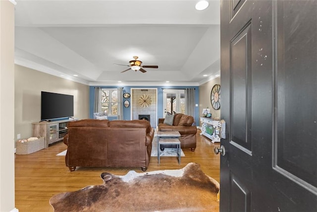 living area featuring a ceiling fan, a raised ceiling, a fireplace, and light wood-style flooring