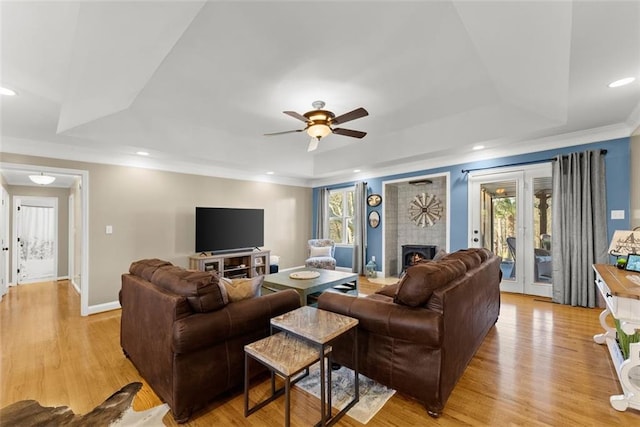 living room with light wood-style floors, a lit fireplace, a tray ceiling, and recessed lighting